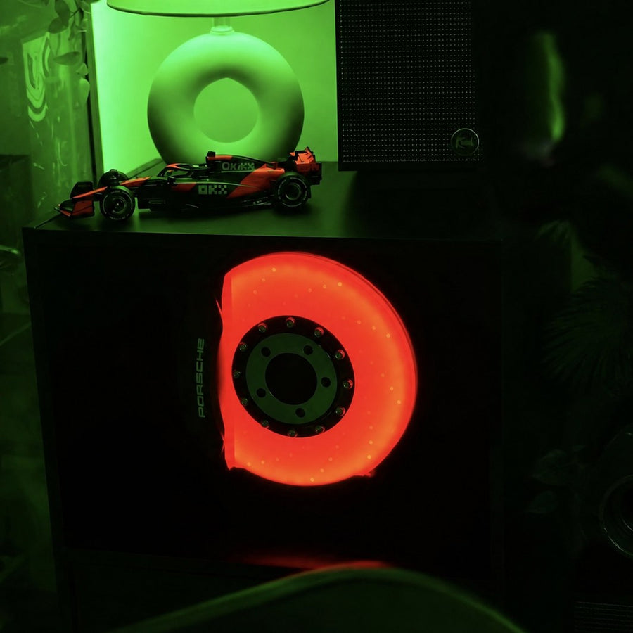 Customer photo: brake disc lamp glowing orange on a desk setup with an F1 model car and a green lamp behind