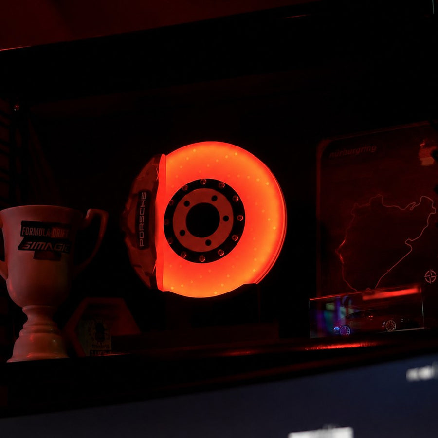 Customer photo: brake disc lamp glowing orange on a display shelf beside a Formula Drift trophy and Nürburgring track art