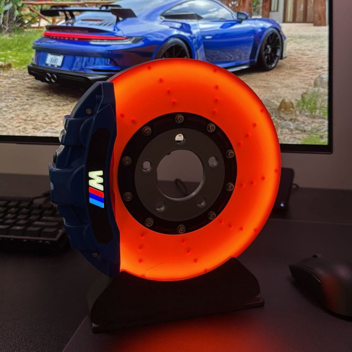 Silver brake disc lamp glowing orange on a desk beside a keyboard and monitor